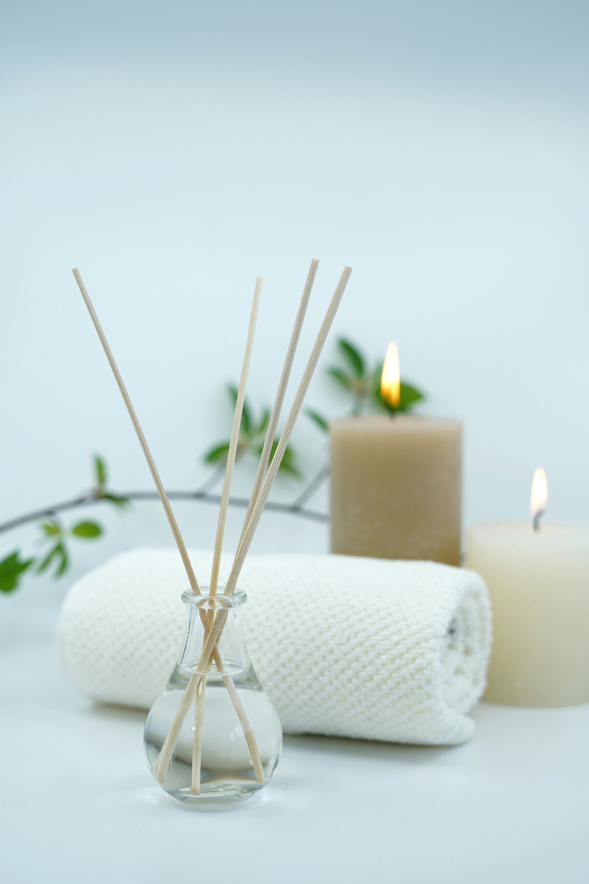 A reed diffuser with wooden sticks, a rolled white towel, and two lit candles